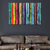 A colourful abstract canvas wall art stripe painting featuring vertical stripes of red, orange, yellow, green, blue, pink, and black, displayed on a dark grey wall above a brown leather sofa.