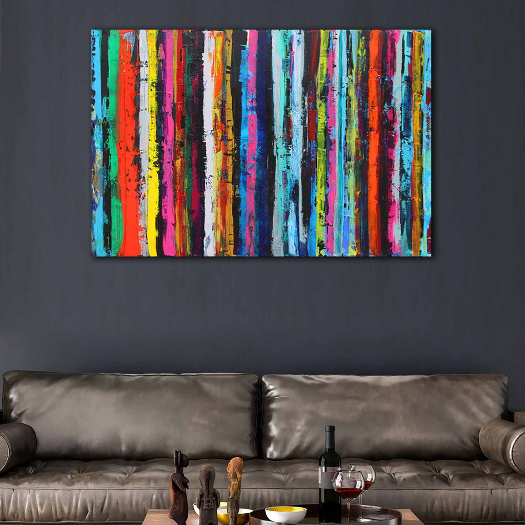 A colourful abstract canvas wall art stripe painting featuring vertical stripes of red, orange, yellow, green, blue, pink, and black, displayed on a dark grey wall above a brown leather sofa.