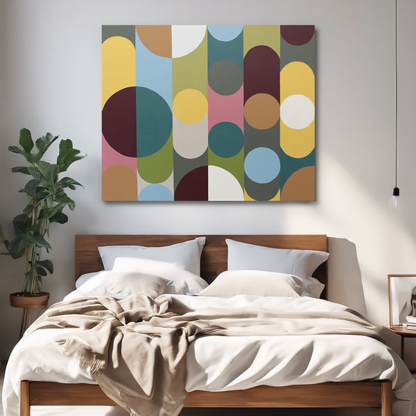 A square abstract wall art painting with overlapping circles and arcs in muted yellow, teal, olive green, burgundy, pink, tan, and cream, displayed above a wooden bed in a modern bedroom setting.