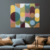 A square abstract wall art painting with overlapping circles and arcs in mustard yellow, teal, olive green, dusty pink, brown, cream, and burgundy, displayed above a blue-grey sofa with brown pillows in a living room setting.