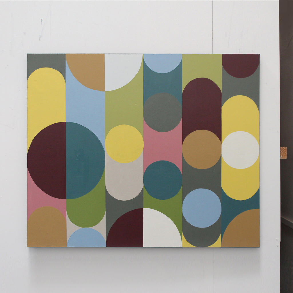 An abstract geometric canvas print featuring overlapping circles and semi-circles in muted colors including yellow, teal, olive green, pink, brown, blue, white, and maroon, displayed on a white wall.