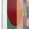 Close-up side view of a framed abstract art painting from AW Modern Art featuring large overlapping circles in red, orange, green, purple, pink, and white on a light background.