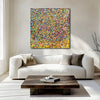 Rainbow Showers - A square abstract canvas painting with a dense multi-colour confetti pattern hangs on a beige wall above a modern white sofa in a bright, sunlit living room.