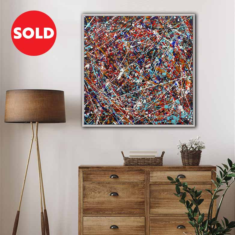 A framed abstract canvas painting with a colourful paint splatter design is displayed on a light grey wall above a wooden dresser in a styled room setting. A red circular 'SOLD' badge is overlaid in the top left corner.