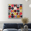 A framed abstract square wall art print with overlapping circles in red, yellow, gray, black, and white, displayed above a navy blue sofa in a modern living room setting.