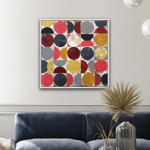 A framed abstract square wall art print with overlapping circles in red, yellow, gray, black, and white, displayed above a navy blue sofa in a modern living room setting.