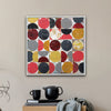 A framed abstract art painting featuring a grid of colourful circles in red, yellow, gray, and maroon, displayed on a beige wall above a wooden side table in a styled room setting.