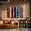 A large rectangular canvas painting featuring vertical multi-colored brushstroke stripes in red, orange, yellow, green, blue, purple, and pink, displayed on a brick wall above a brown leather sofa in a modern living room.