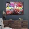 A large rectangular abstract canvas painting with vibrant, textured brushstrokes in red, pink, yellow, blue, white, and brown, displayed on a dark gray wall above a dark wood credenza in a styled living room setting.
