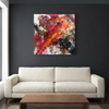 Fire Starter  - A large abstract canvas painting with vibrant red, orange, yellow, black, and white paint strokes, displayed on a dark charcoal wall above a modern cream coloured sofa.