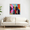 A square framed abstract geometric wall art painting with a colourful mosaic pattern hangs above a light beige sofa in a bright, modern living room.