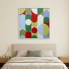 Geo Pop Lines No 2 - A square framed wall art painting with an abstract mid-century modern geometric pattern of overlapping circles and arches in red, green, blue, yellow, and white, hanging above a neatly made bed in a minimalist bedroom.