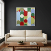Geo Pop Lines No 2 - A square framed abstract wall art painting with overlapping circles and arcs in red, green, blue, yellow, and white, displayed above a cream sofa in a dark living room. A small dimension marker reads 22cm.