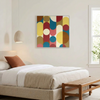 A square wall art painting with a mid-century modern abstract design of overlapping circles and arcs in mustard yellow, teal blue, coral pink, and terracotta red, hanging above a neatly made bed in a bright, modern bedroom.