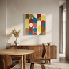 A framed abstract geometric wall art painting with large overlapping circles in yellow, blue, red, pink, and tan, displayed above a wooden sideboard in a modern dining room setting.