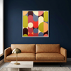 Geo Pop Lines No 6 - A square framed wall art painting with a colourful mid-century modern geometric pattern of overlapping arches and circles, displayed on a dark navy blue wall above a tan leather sofa with a brass table lamp.