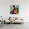 Geo Blocks 1 - A colourful geometric wall art painting hangs above a cream sofa in a modern living room. The artwork features an abstract multi-colour pattern of triangles and polygons in pink, blue, orange, yellow, green, black, and grey.