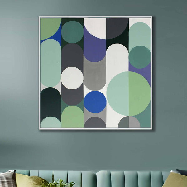 A square framed abstract wall art painting with overlapping circles and arcs in muted green, blue, grey, white, and black, hanging on a blue-grey wall above a tufted sofa.