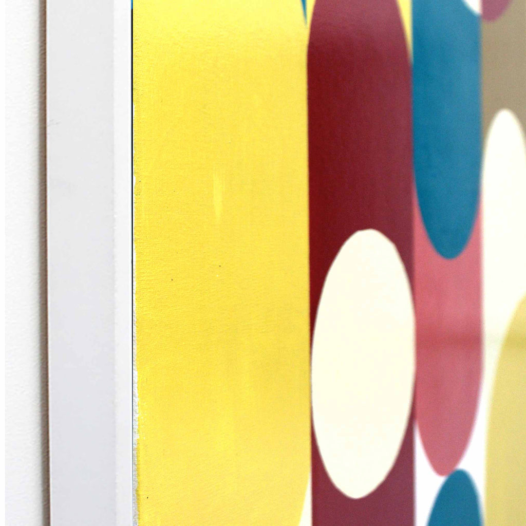 Close-up of a colorful abstract artwork featuring large overlapping circles in yellow, burgundy, teal, pink, and cream, with a white vertical frame or wall edge visible on the left.