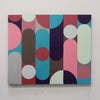 A square abstract canvas painting featuring a mid-century modern geometric pattern of vertical bars and rounded shapes in pink, teal, brown, red, gray, and white, hung on a white wall.