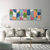 A wide rectangular abstract wall art piece with overlapping semicircles and arcs in muted blue, teal, pink, orange, green, and cream, displayed above a light beige sofa in a bright modern living room.