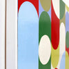 Close-up of a colourful abstract wall art painting with overlapping rounded arches and circles in light blue, green, red, yellow, and white, shown against a white wall.