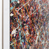 Side view close-up of a framed abstract drip-style painting with energetic splatters and drips in red, blue, white, black, and gold tones, shown against a white wall.