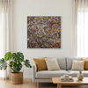 A large framed abstract canvas painting with splatters of red, yellow, white, and black paint hangs on a light gray wall above a modern light gray sofa in a bright living room with a potted green plant and a wooden coffee table.