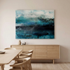 Nordic Mist - An abstract canvas painting with shades of teal, blue, and white hangs on a beige wall above a light wood sideboard and dining table with chairs.