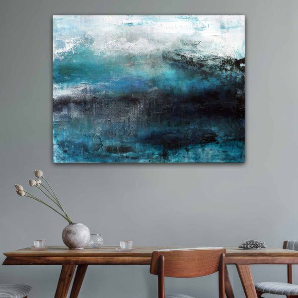 Abstract canvas wall art painting featuring textured brushstrokes of teal, blue, black, and white, displayed on a grey wall above a wooden dining table with chairs and a vase.