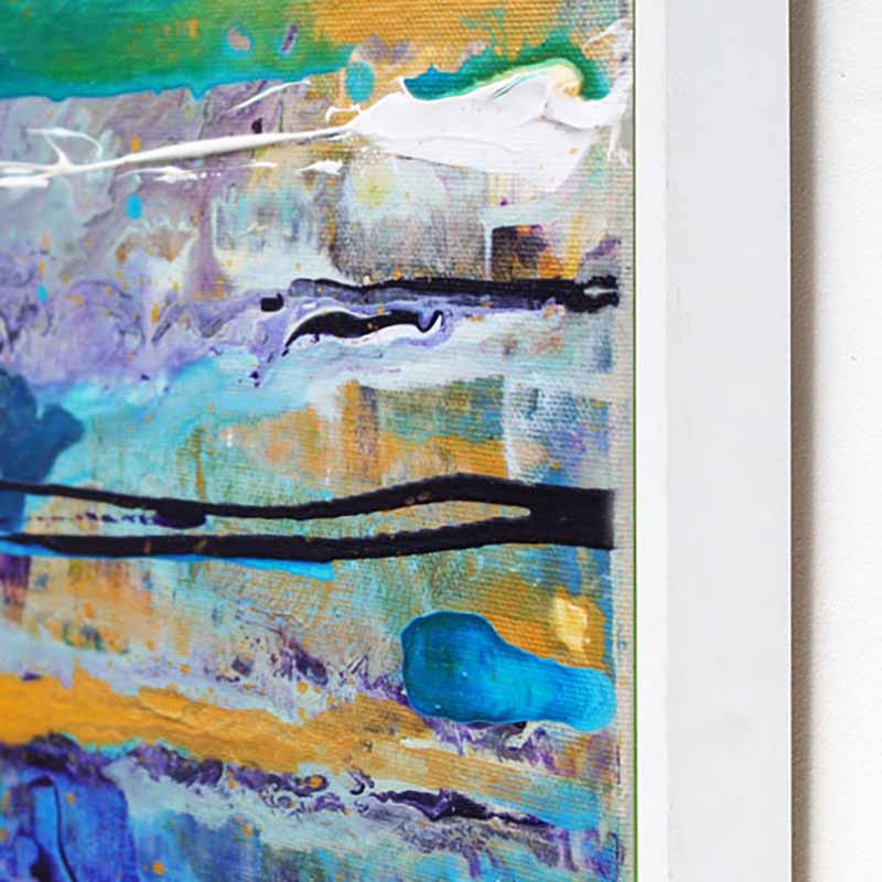 Close-up of an abstract canvas painting Ocean mist by Andy Watt with textured impasto brushstrokes in blue, teal, white, gold, purple, and black, shown with a white frame edge on a light wall.