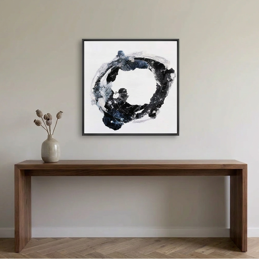 Orbital - A square framed abstract wall art painting hangs above a wooden console table against a light beige wall. The artwork features a black, gray, and white circular brushstroke design.