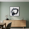 Orbital - A framed abstract black, white, and gray brushstroke artwork hangs on a sage green wall above a light wood sideboard in a modern dining room setting.