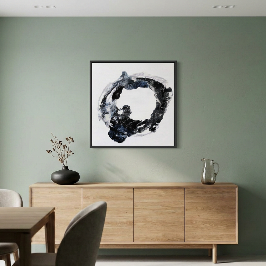 Orbital - A framed abstract black, white, and gray brushstroke artwork hangs on a sage green wall above a light wood sideboard in a modern dining room setting.