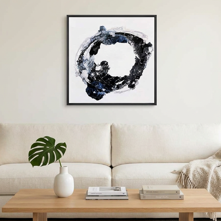 Orbital - A framed abstract wall art painting featuring a black and blue circular brushstroke design on a white background, hanging above a modern beige sofa in a bright, minimalist living room.