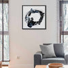 A framed abstract black, white, and blue circular painting called Orbital hanging on a beige wall above a grey sofa in a modern living room setting.