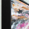Close-up of a framed abstract painting showing a thick black frame and textured brushstrokes in white, gray, black, gold, and pink.