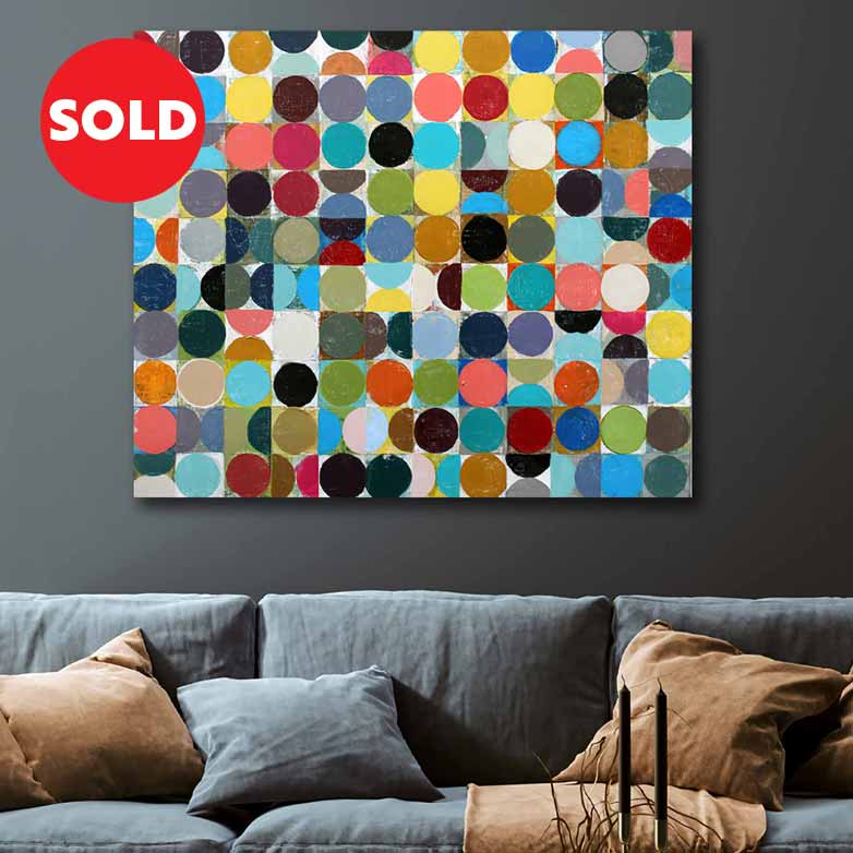 A colourful abstract canvas painting featuring a grid of multi-coloured circles on a light background, shown hanging on a dark grey wall above a grey sofa with brown and blue pillows. A red circular 'SOLD' badge is overlaid in the top-left corner.