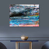 Abstract canvas wall art featuring a colorful landscape-like composition with blue, pink, black, gray, and white brushstrokes, displayed on a dark gray wall above a small table with a bowl.