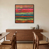 Tulum - A framed abstract canvas painting with vibrant horizontal stripes in red, orange, pink, green, and blue, hanging on a beige wall above a mid-century modern wooden credenza in a dining room setting.