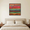 Tulum - A framed abstract canvas painting with vibrant horizontal brushstrokes of red, orange, yellow, green, and blue, displayed on a beige wall above a neatly made bed in a modern bedroom setting.
