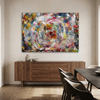 Turbulence - A large abstract canvas painting featuring a vibrant, swirling circular pattern in multiple colours, displayed on a beige wall above a wooden sideboard in a modern dining room setting.