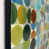 Close-up of a framed abstract geometric painting featuring painted circles in green, yellow, blue, brown, gray, and beige on a white background, with a black frame visible against a white wall.