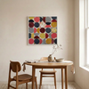 Vintage Spheres No 6 - A large square abstract wall art painting with a grid of red, yellow, navy, grey, and cream circles hangs above a light wood dining table with two wooden chairs in a bright, modern room.