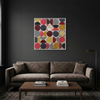 Vintage Spheres No 6 - A large square framed abstract wall art painting with a grid of red, yellow, grey, black, and white circles, displayed above a dark brown velvet sofa in a modern living room setting.