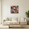 Vintage Spheres No 6 - A large square framed wall art painting with a grid of painted circles in red, yellow, grey, navy, and white, displayed above a cream sofa in a bright living room.