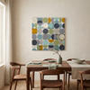 Vintage Spheres No 7 - A large square canvas wall art painting featuring a modern geometric pattern of overlapping circles in muted teal, navy, olive green, mustard yellow, and grey, displayed on a beige wall above a wooden dining table with chairs.