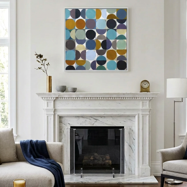 A square framed abstract art painting featuring a geometric pattern of overlapping circles in muted blue, yellow, purple, and grey, displayed on a white wall above a white marble fireplace mantel in a modern living room setting.