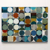 An abstract geometric painting featuring a grid of squares with painted circles and semi-circles in muted blue, teal, gray, brown, olive, cream, and rust tones, hung on a white wall.