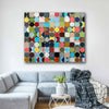A large landscape canvas wall art print featuring a colourful grid of textured circles, displayed on a white wall above a modern grey sectional sofa in a living room setting.